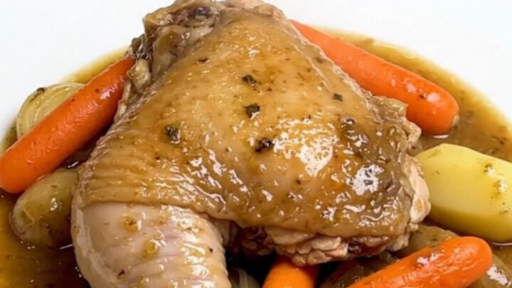 A slow cooker filled with chicken thighs, carrots, potatoes, and onions in a rich herb gravy.