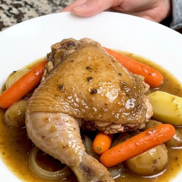 A slow cooker filled with chicken thighs, carrots, potatoes, and onions in a rich herb gravy.