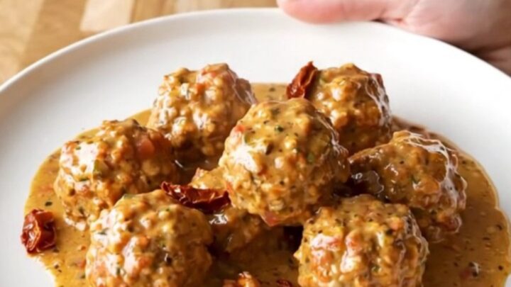 A close-up of turkey meatballs in a creamy sun-dried tomato sauce inside a slow cooker, with a spoon lifting one out.