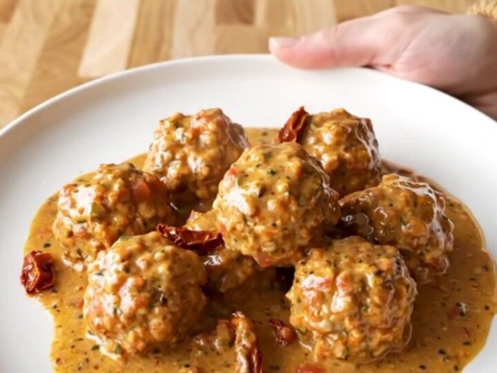 A close-up of turkey meatballs in a creamy sun-dried tomato sauce inside a slow cooker, with a spoon lifting one out.
