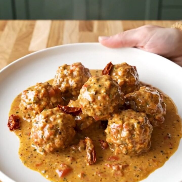 A close-up of turkey meatballs in a creamy sun-dried tomato sauce inside a slow cooker, with a spoon lifting one out.
