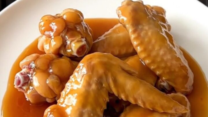A close-up of slow cooker hot honey chicken wings arranged on a white plate, glistening with a thick, spicy-sweet glaze.