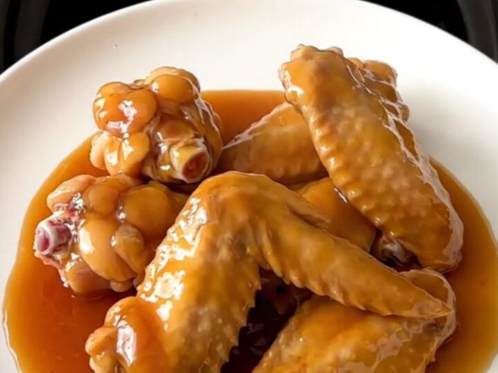 A close-up of slow cooker hot honey chicken wings arranged on a white plate, glistening with a thick, spicy-sweet glaze.