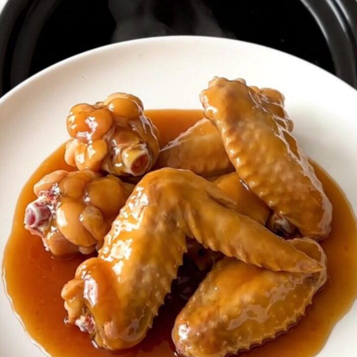 A close-up of slow cooker hot honey chicken wings arranged on a white plate, glistening with a thick, spicy-sweet glaze.