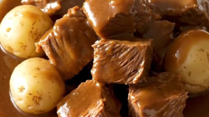 A close-up of tender beef tips and baby potatoes in a rich, savory brown au jus gravy served in a white bowl.