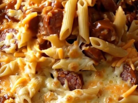 A top-down view of a rectangular baking dish filled with penne pasta, smoked sausage coins, barbecue sauce