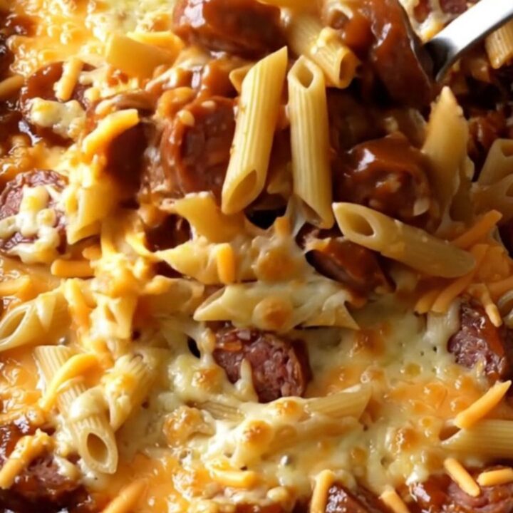 A top-down view of a rectangular baking dish filled with penne pasta, smoked sausage coins, barbecue sauce