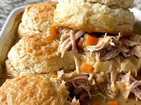 A top-down view of a rectangular baking dish filled with creamy chicken, carrots, and peas topped with raw biscuit dough.