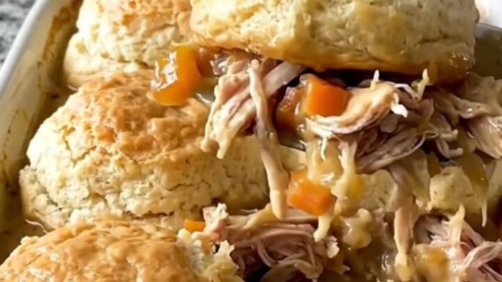 A top-down view of a rectangular baking dish filled with creamy chicken, carrots, and peas topped with raw biscuit dough.