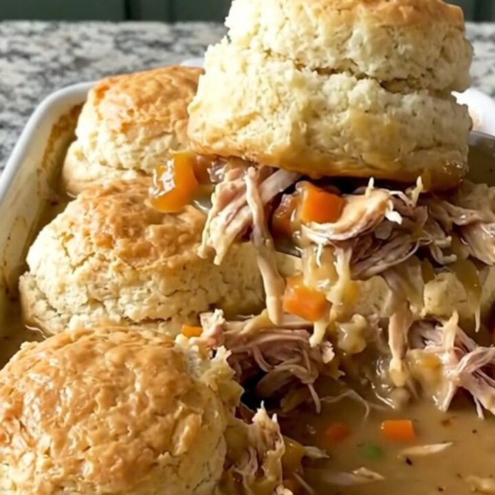A top-down view of a rectangular baking dish filled with creamy chicken, carrots, and peas topped with raw biscuit dough.