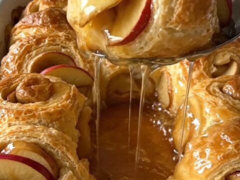 A top-down view of rows of crescent dough-wrapped apple wedges in a white baking dish ready for the oven.