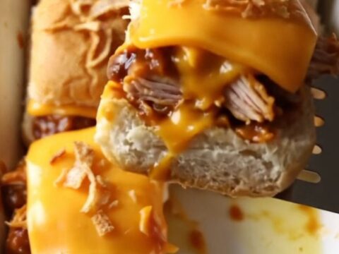 A rectangular baking dish filled with golden brown BBQ chicken sliders topped with crispy fried onions.