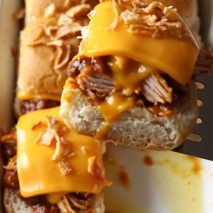 A rectangular baking dish filled with golden brown BBQ chicken sliders topped with crispy fried onions.