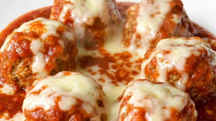 A top-down view of tender chicken meatballs simmering in a rich marinara sauce inside a black slow cooker.
