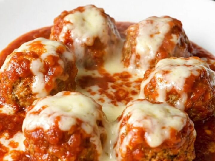 A top-down view of tender chicken meatballs simmering in a rich marinara sauce inside a black slow cooker.
