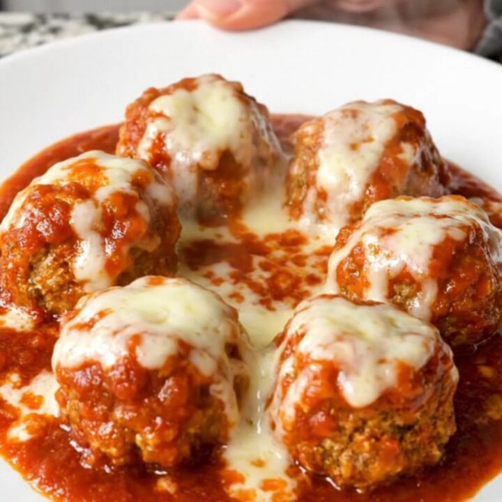 A top-down view of tender chicken meatballs simmering in a rich marinara sauce inside a black slow cooker.