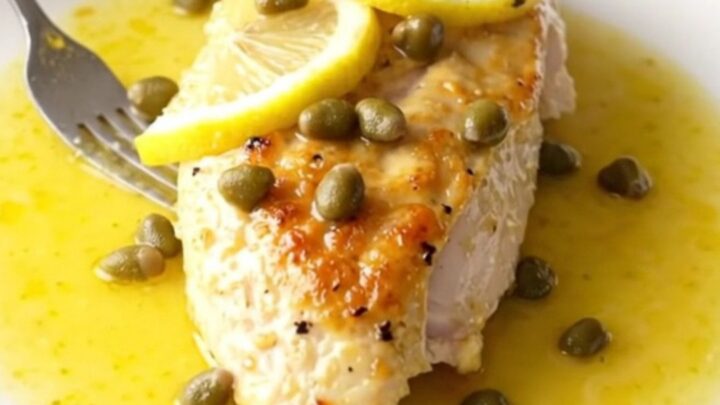 A high-angle view of tender, braised chicken breasts in a slow cooker with lemon slices and capers.