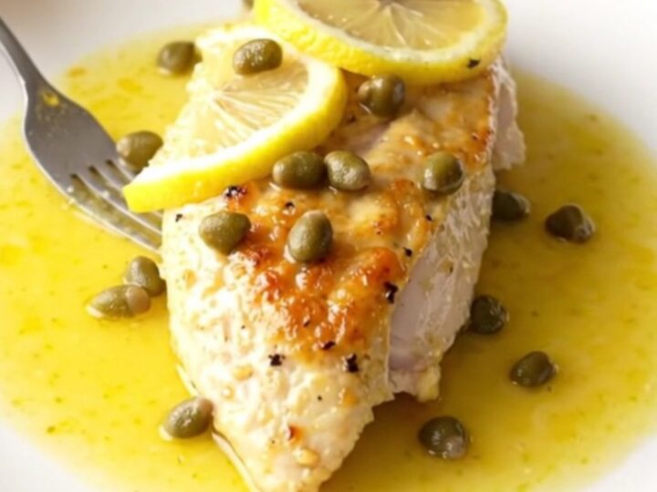A high-angle view of tender, braised chicken breasts in a slow cooker with lemon slices and capers.