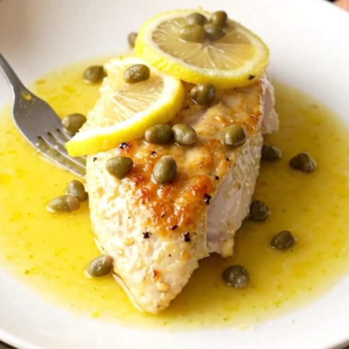 A high-angle view of tender, braised chicken breasts in a slow cooker with lemon slices and capers.