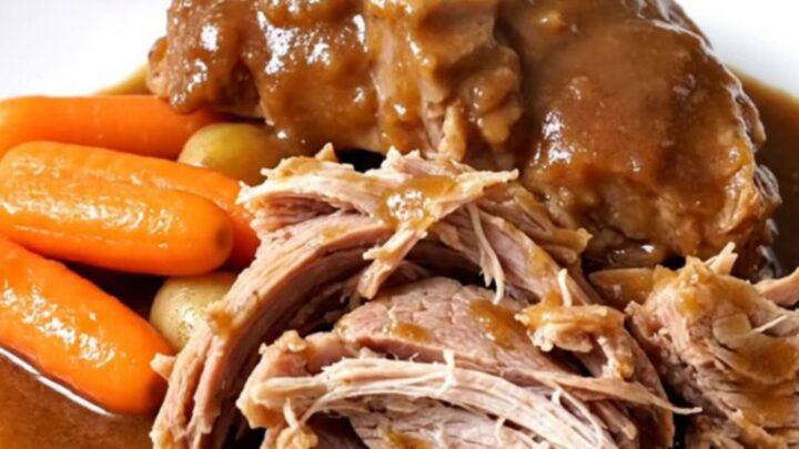 A tender, slow-cooked pork shoulder roast surrounded by baby carrots and potatoes in a black slow cooker insert.