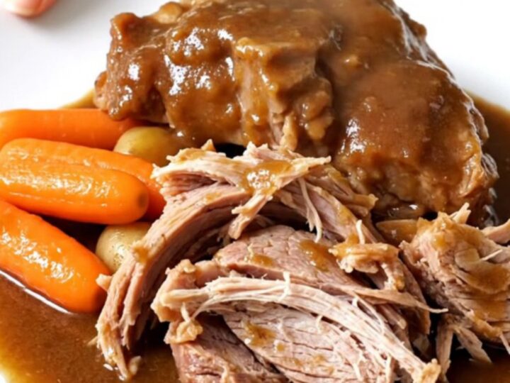 A tender, slow-cooked pork shoulder roast surrounded by baby carrots and potatoes in a black slow cooker insert.