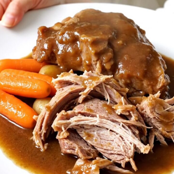 A tender, slow-cooked pork shoulder roast surrounded by baby carrots and potatoes in a black slow cooker insert.
