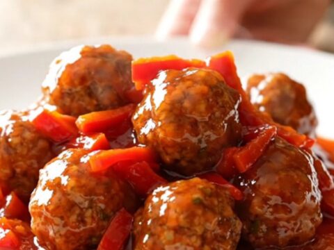 A slow cooker filled with turkey meatballs glazed in a glossy, red pepper jelly sauce.