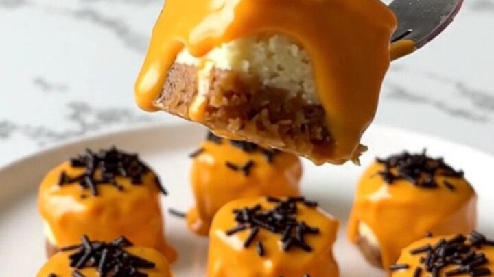 A close-up of vibrant orange dipped cheesecake bites with black sprinkles on a white plate.