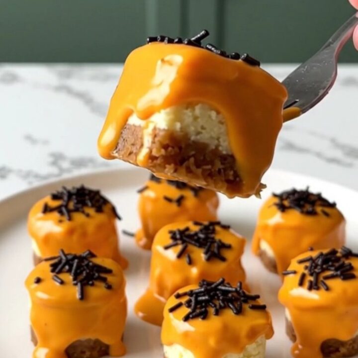 A close-up of vibrant orange dipped cheesecake bites with black sprinkles on a white plate.