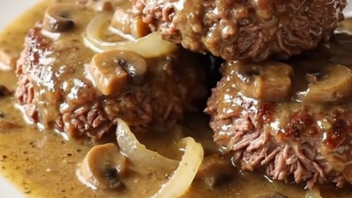 A close-up of a slow cooker filled with beef patties and creamy mushroom gravy.