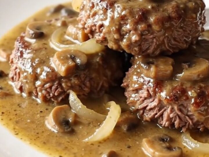 A close-up of a slow cooker filled with beef patties and creamy mushroom gravy.