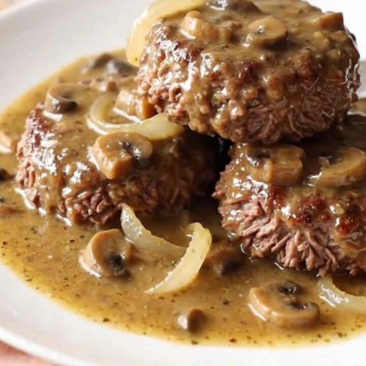 A close-up of a slow cooker filled with beef patties and creamy mushroom gravy.