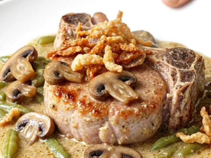 A plate of slow-cooked pork chops covered in creamy mushroom sauce and green beans with crispy onions.