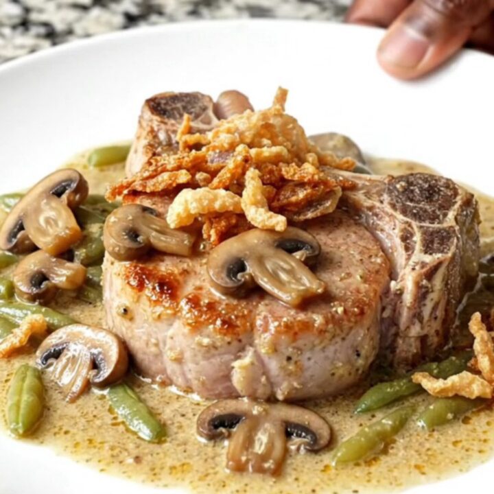 A plate of slow-cooked pork chops covered in creamy mushroom sauce and green beans with crispy onions.