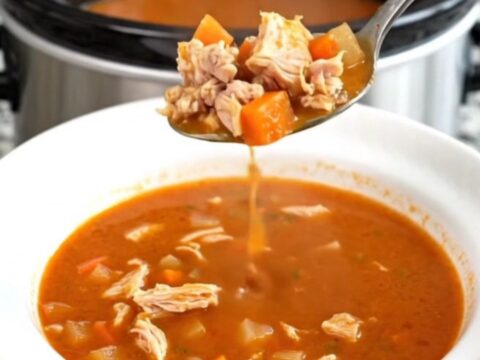 A black slow cooker filled with a hearty ground turkey and vegetable soup on a granite countertop.