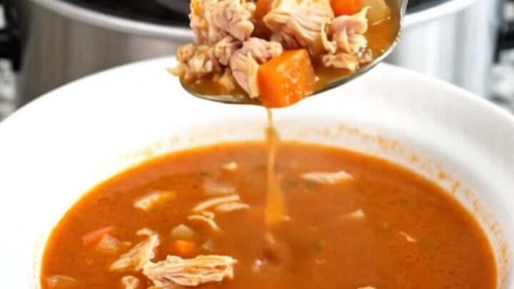 A black slow cooker filled with a hearty ground turkey and vegetable soup on a granite countertop.