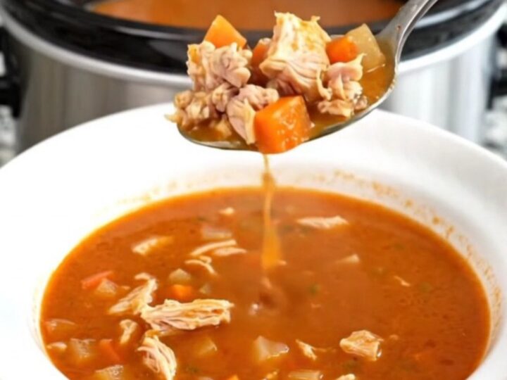 A black slow cooker filled with a hearty ground turkey and vegetable soup on a granite countertop.