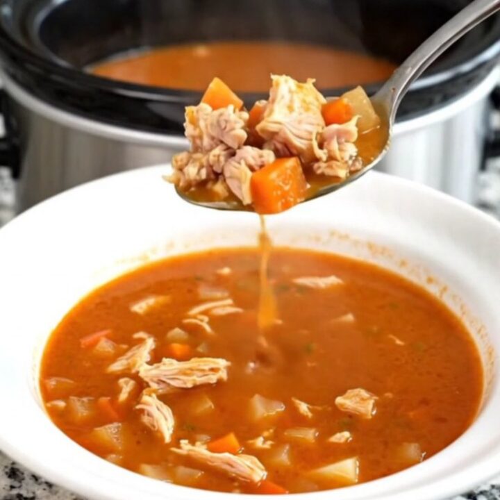 A black slow cooker filled with a hearty ground turkey and vegetable soup on a granite countertop.