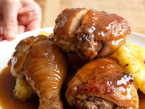 A stainless steel slow cooker filled with chicken thighs, pineapple chunks, and a rich amber glaze.
