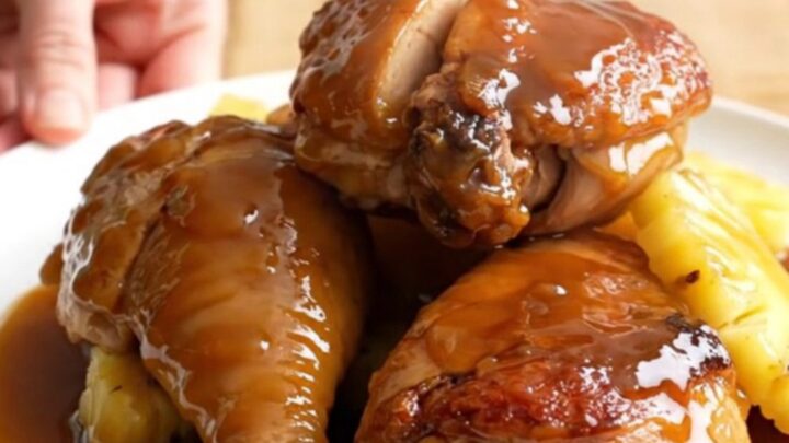 A stainless steel slow cooker filled with chicken thighs, pineapple chunks, and a rich amber glaze.