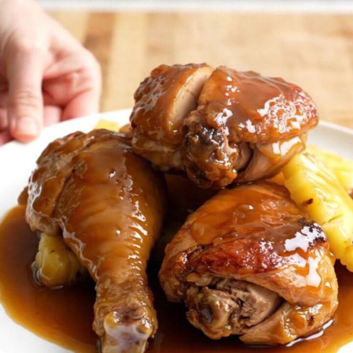 A stainless steel slow cooker filled with chicken thighs, pineapple chunks, and a rich amber glaze.
