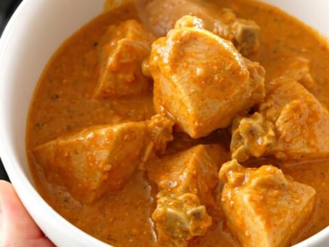 A bowl of creamy chicken tikka masala with a rich orange sauce and tender chicken pieces.