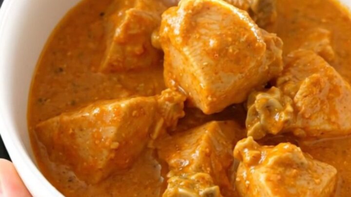 A bowl of creamy chicken tikka masala with a rich orange sauce and tender chicken pieces.
