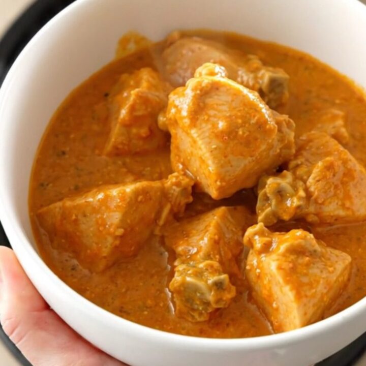 A bowl of creamy chicken tikka masala with a rich orange sauce and tender chicken pieces.