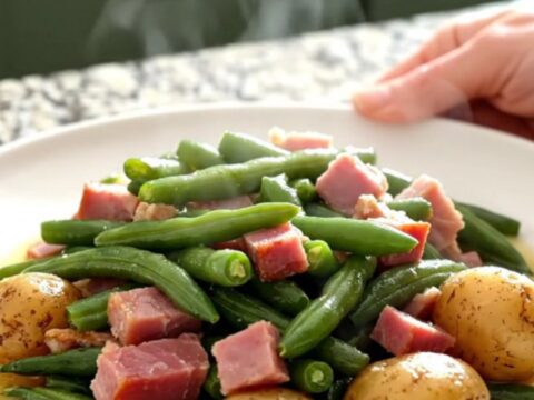 A slow cooker filled with chunks of cooked ham, green beans, and potatoes in a savory broth.