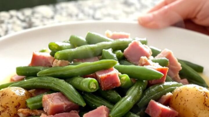 A slow cooker filled with chunks of cooked ham, green beans, and potatoes in a savory broth.