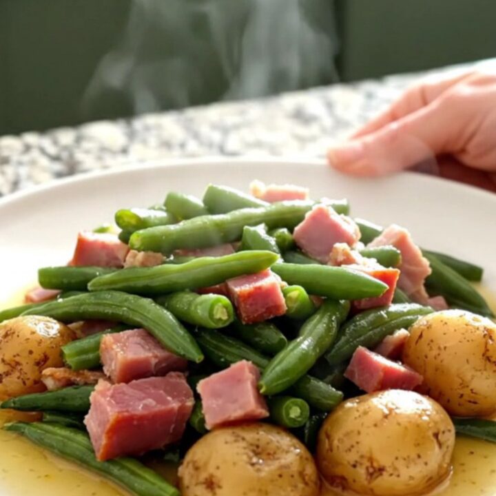 A slow cooker filled with chunks of cooked ham, green beans, and potatoes in a savory broth.