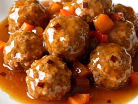 A top-down view of a black slow cooker filled with glazed meatballs and diced red bell peppers.