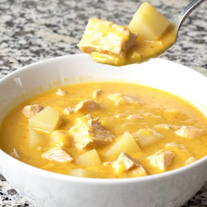 A bowl of creamy cheesy chicken potato soup with chunks of chicken and potatoes, garnished with fresh herbs.