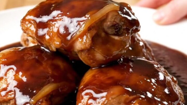 A close-up of slow-cooked chicken thighs in a rich, dark cherry cola glaze on a white plate.